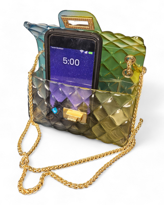 An opened quilted jelly crossbody bag in an ombre design of blue and green shades, showing a phone inside, with a gold chain strap and clasp.