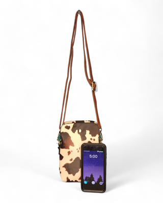 A cow print crossbody bag with a brown and cream cowhide pattern, featuring a rich brown leather strap.