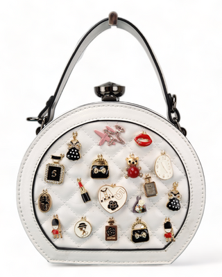 White crossbody handbag with a quilted face and adorned with charms.