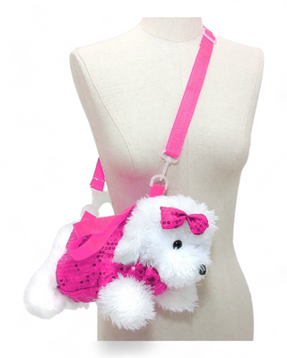 A plush white dog crossbody bag with a magenta glittery dress and a magenta bow on its head. It has a magenta adjustable strap and is positioned on a mannequin