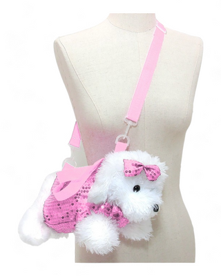 A plush white dog crossbody bag with a pink glittery dress and a matching pink bow on its head. The bag features a pink adjustable strap and is displayed on a mannequin