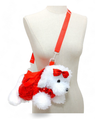 A plush white dog crossbody bag dressed in a red glittery outfit with a red bow on its head. The bag includes a red adjustable strap, presented on a mannequin