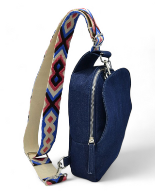 Denim sling bag with a colorful, geometric-patterned strap, featuring a zippered side pocket.