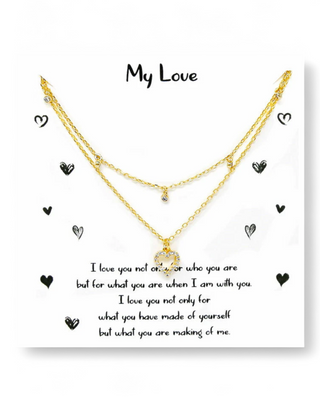 Layered gold necklace with a crystal heart pendant, displayed on a "My Love" message card with black heart doodles and a romantic quote.