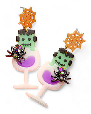  Whimsical Monster Drink Earrings, showcasing Frankenstein's monster head on top of a purple-filled cocktail glass. Decorated with a sparkly spider and a bright orange web