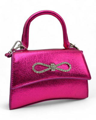 A bold fuchsia handbag with a shiny finish, accented by a sparkling rhinestone bow on the front. The bag features a top handle and an optional crossbody strap for easy wear.