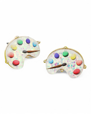 A pair of artist palette stud earrings with a glittery resin base, multicolored paint spots, and a miniature brush detail, set in a gold-tone finish.