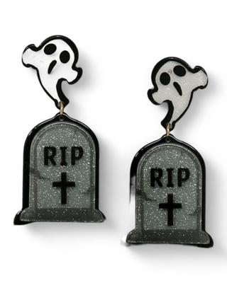 A pair of Halloween-themed earrings featuring a white ghost emerging from a sparkling black tombstone marked "RIP,"