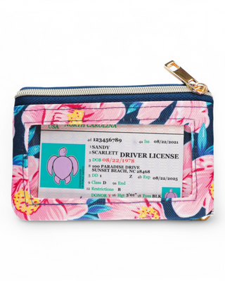 A small zippered wallet with a colorful floral pattern, featuring a clear ID window on one side and a gold pineapple emblem on the back.