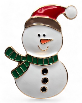 A snowman-shaped brooch featuring a red Santa hat, green scarf, and smiling face. The snowman has black buttons and an orange nose, with a glossy enamel finish