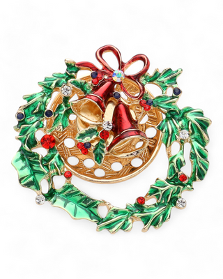 A festive magnetic brooch featuring a gold and green wreath with red bells, holly leaves, and sparkling rhinestones. The brooch has a magnetic back, making it pinhole-free.