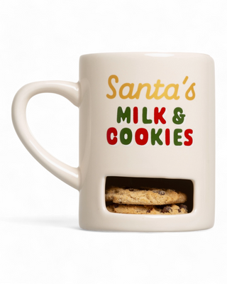 A white mug featuring the phrase "Santa's Milk & Cookies" in festive red, green, and yellow lettering, with a built-in cookie compartment at the bottom holding chocolate chip cookies.