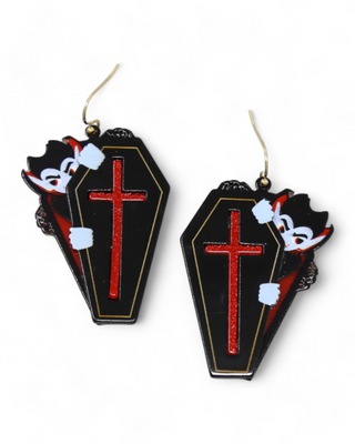 Dangling earrings shaped like caskets, each with a red cross and an illustration of Dracula peeking out, set against a black background.