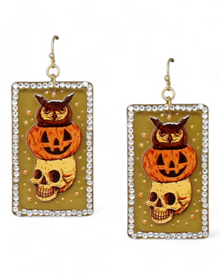 Halloween earrings featuring an owl perched on top of a jack-o'-lantern, which is stacked above a skull, all within a rectangular frame adorned with rhinestones