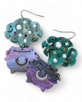 A pair of earrings featuring lavender clouds adorned with colorful gems and stars, attached to black cauldrons with crescent moons,