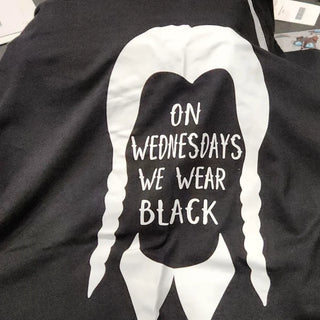 "Black T-shirt with 'On Wednesdays We Wear Black' printed in white capital letters, inspired by Wednesday Addams' style."