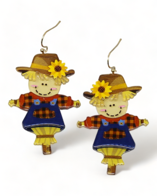 A pair of scarecrow earrings featuring a cute scarecrow design with a plaid shirt, blue overalls, and a sunflower-adorned hat.