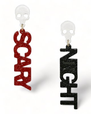 A pair of Halloween-themed earrings with glittery text reading "SCARY" in red and "NIGHT" in black, topped with white skull studs.